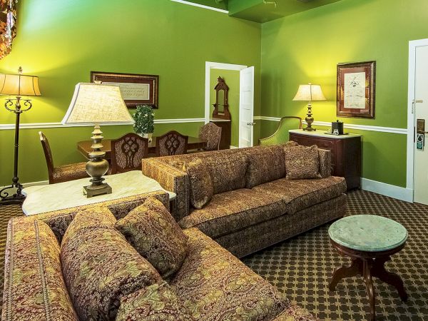 A cozy room with green walls, patterned couches, multiple lamps, a table with a white top, and framed art and decor on the walls.