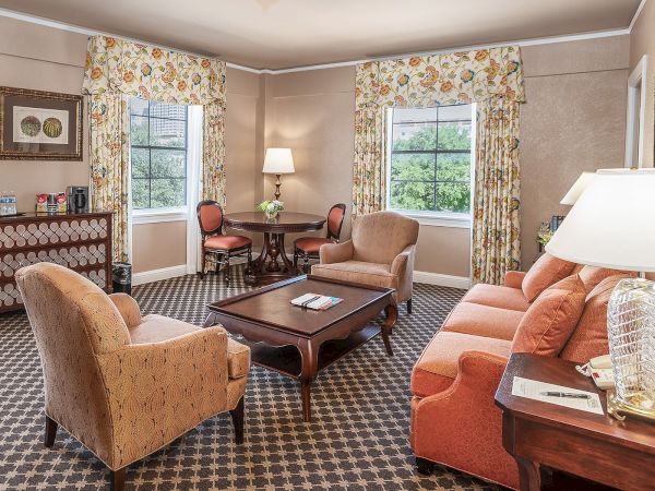 The image shows a cozy living room with upholstered furniture, a coffee table, and windows with floral curtains.