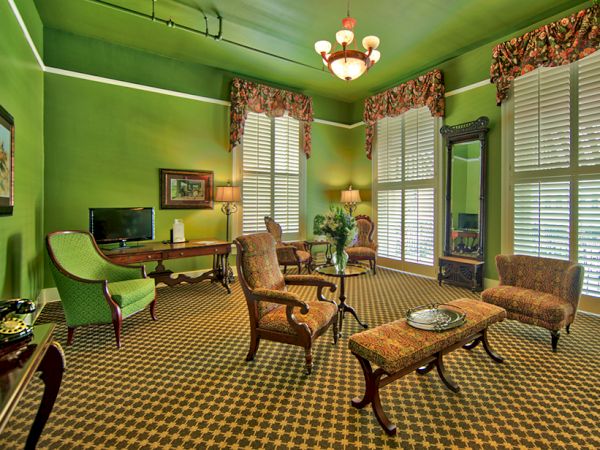 A vibrant green room with classic furniture, large windows, patterned carpet, a chandelier, and decorative plants creating a cozy atmosphere.