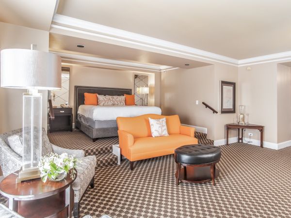 A spacious bedroom with a bed, orange sofa, patterned carpet, lamp, and chairs, creating a cozy and elegant atmosphere.