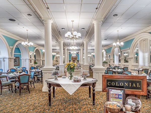 A cozy, elegant dining room with teal walls, white columns, chandeliers, and a central table set for service in a classic hotel/restaurant.