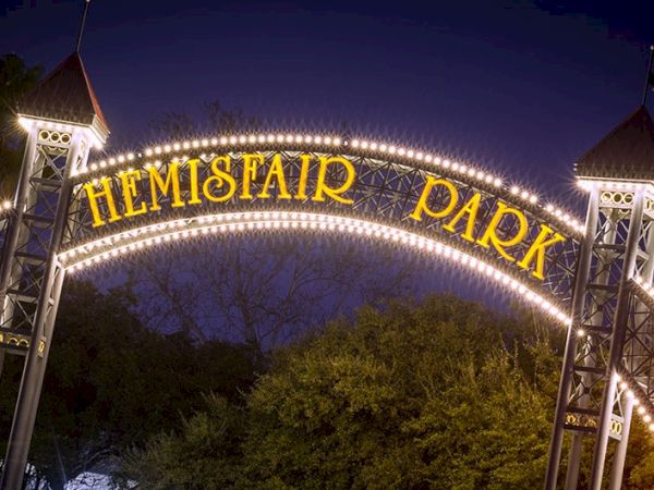 A glowing arch reads &ldquo;Hemispair Park&rdquo; at night with bright lights, towers on both sides, and trees beneath the dark sky.