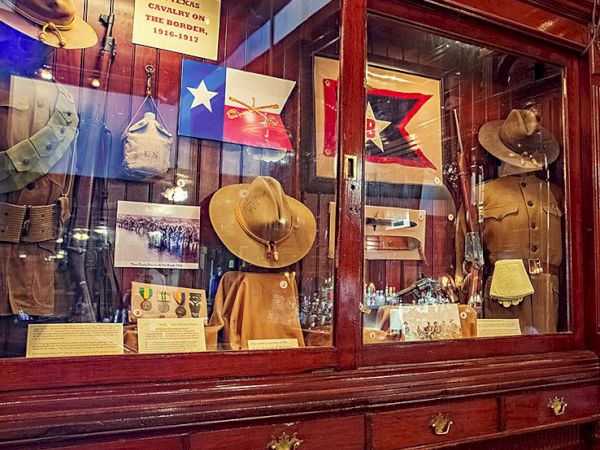 A wooden display case with Texas flags, cowboy hats, and memorabilia; a patriotic storefront vignette inside glass with signs and hats, yes.