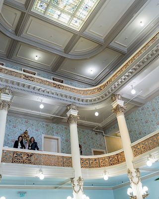 Luxurious interior with tall white columns, ornate railings, chandelier lighting, and a high decorative ceiling in a grand hall, elegant and opulent.