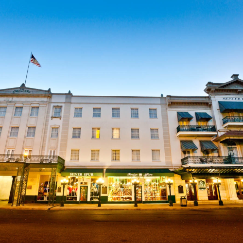 A row of elegant shops and a grand white building with an American flag, lit storefronts, and a clear evening sky, vibrant and inviting.