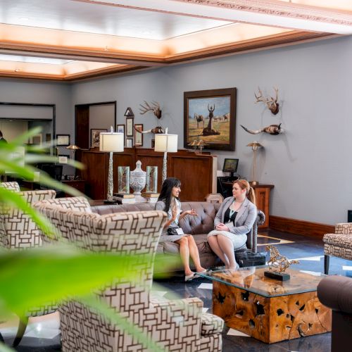 A cozy, sunlit outdoor living space with potted plants, wicker furniture, a coffee table, and a shaded seating area near a brick wall.