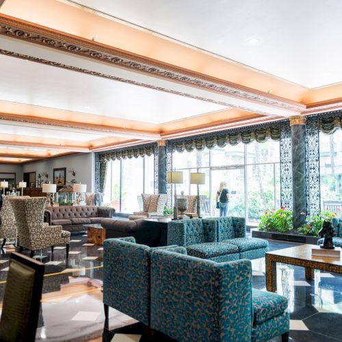 A modern open-plan office with glass walls, desks in rows, people working, and plenty of natural light from large windows.