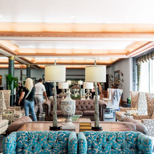 A bright, open-plan living area with mid-century chairs, a sofa, shelves, and people browsing decor items in a showroom-like space.