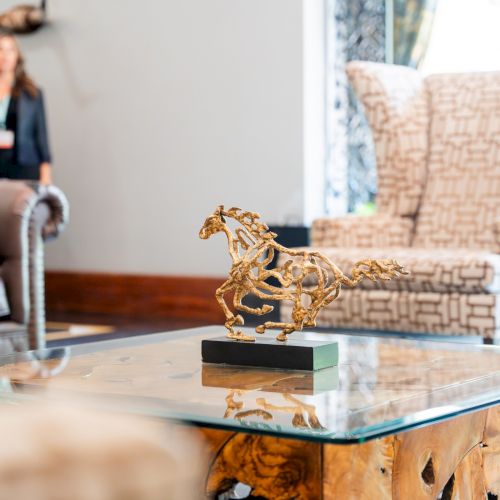 A cozy living room with a patterned rug, a wooden coffee table, a sofa, a potted plant, and a person standing near a window.