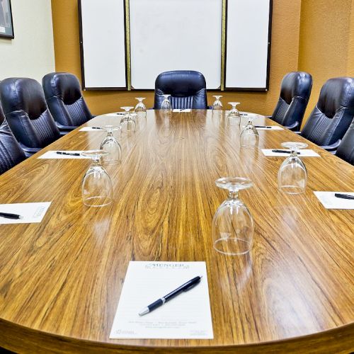 A long, oval conference table with eight chairs, note papers, pens, and empty glasses set for a meeting, in a polished boardroom.