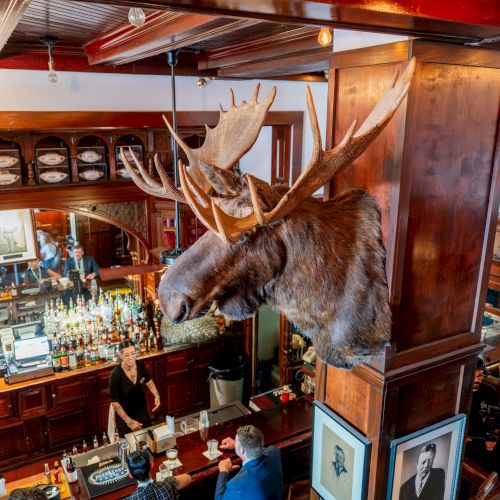 A busy bar scene with shelves of bottles, warm lighting, and people chatting&mdash;feeling vibrant and social in a cozy, bustling venue.