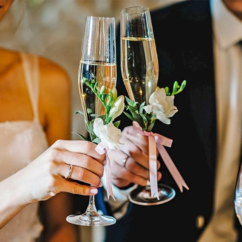 Two people clink champagne flutes at a wedding or celebrations, festive and romantic.